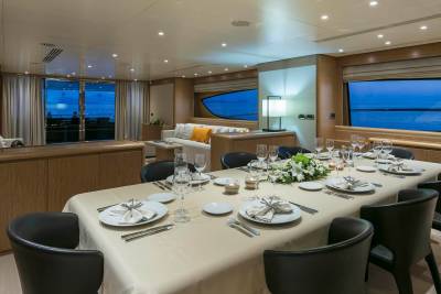 A formal dining table is set for a luxurious meal aboard a yacht, overlooking a serene twilight sea.