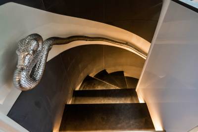 A metallic snake sculpture coils elegantly around a modern spiral staircase, adding a dramatic touch to the interior design.