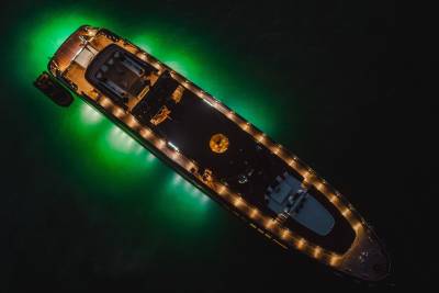 A luxurious yacht glows with emerald lights as it rests on dark, tranquil waters.