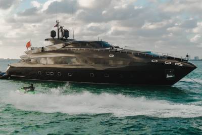 A jet ski cuts through the turquoise water near a sleek, black yacht under a cloudy sky.