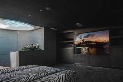 A luxurious yacht is displayed on a large screen in a modern, dimly lit room featuring zebra-print seating.