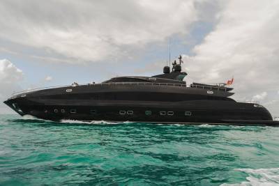 A sleek black yacht glides through turquoise waters under a cloudy sky.