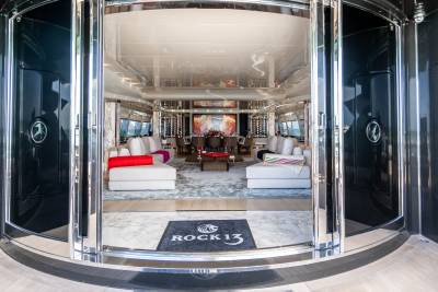 A luxurious yacht interior features a spacious living area with plush white sofas, elegant artwork, and a wine display.