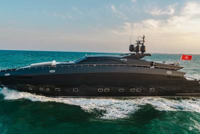 A sleek black yacht named Rock 13 cuts through the turquoise waters under a bright sky.