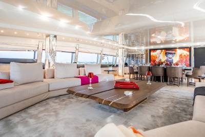 A modern yacht's spacious living area features a large sectional sofa, a unique wooden coffee table, and vibrant artwork.