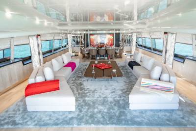 Luxurious yacht interiors feature plush white sofas, a formal dining area, and expansive windows overlooking the serene blue ocean.