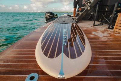 A sleek paddleboard rests on the polished wooden deck of a yacht, ready for adventure on the turquoise waters.