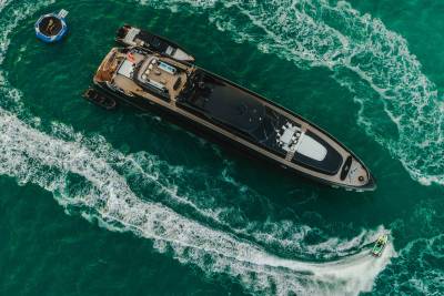 A luxurious yacht cruises through emerald waters, trailed by a jet ski and accompanied by inflatable water toys.