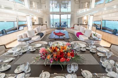 A beautifully set dining table aboard a luxury yacht awaits guests with a vibrant floral centerpiece and stunning ocean views.