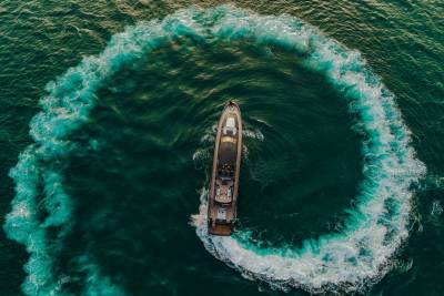 A luxury yacht carves a dramatic turquoise wake through the deep green ocean.