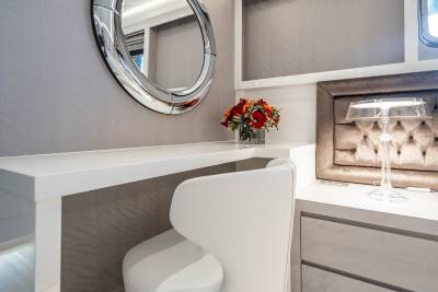 A modern vanity with a white chair and a bouquet of flowers sits beside a tufted headboard and a clear glass lamp.