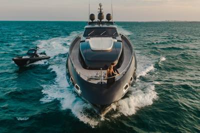 A sleek yacht cuts through the turquoise waves, accompanied by a smaller tender boat, as a couple enjoys the open sea.