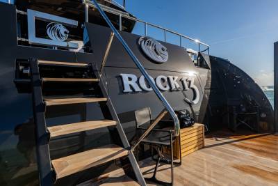 The sleek black yacht "ROCK13" gleams under the sun with its polished chrome accents and wooden deck.