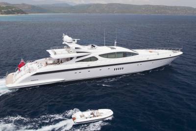 A sleek white yacht cruises through deep blue waters, with a smaller dinghy following close behind.