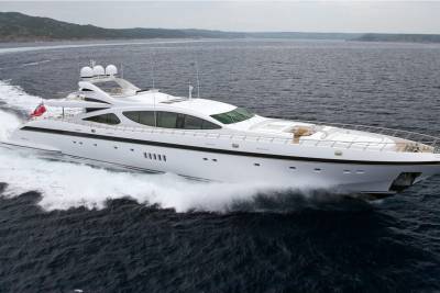 A sleek white yacht cuts through dark, choppy waters, leaving a frothy wake against a backdrop of distant, hazy hills.