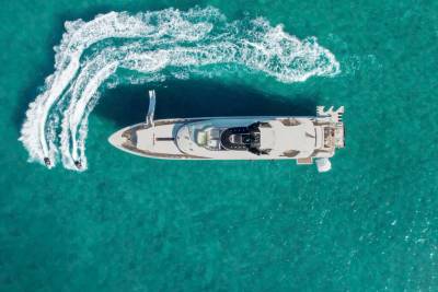 Two jet skis create white wakes as they race around a luxurious yacht anchored in turquoise waters.
