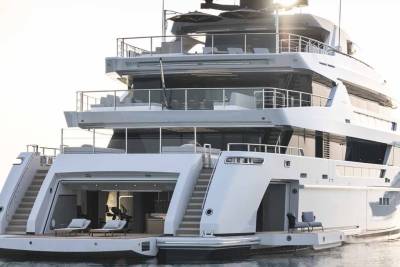 A luxurious superyacht with multiple decks and open-air seating areas rests on calm waters under a bright sky.