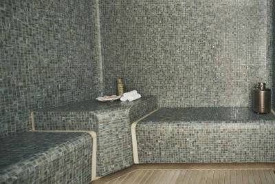 Relax in a mosaic-tiled steam room with smooth wooden flooring and elegant spa accessories.