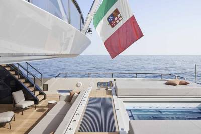 A luxurious yacht deck features a jacuzzi, comfortable seating, and an Italian flag against a clear blue sky.