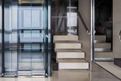 A modern glass elevator and sleek stone staircase create a striking architectural statement in this luxurious interior.