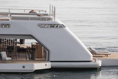 A sleek white yacht with open deck spaces and comfortable seating floats serenely on calm, rippling water.