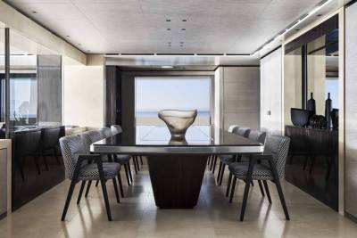 A modern dining room with a large table and chairs overlooks a serene ocean view.