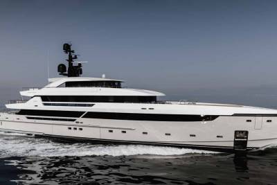 A sleek white superyacht glides through calm waters under a hazy sky.