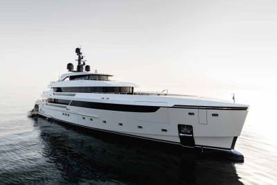 A sleek white superyacht glides through calm waters under a bright, hazy sky.