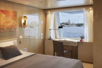 A cozy cabin with a large window offers a serene view of a historic coastal town and the tranquil sea.