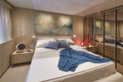 A luxurious bedroom aboard a yacht features a cozy bed draped with a blue throw, a modern bedside table, and a striking abstract painting.