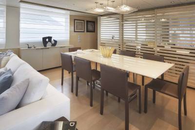 A modern dining room features a long table with brown chairs, a white sofa, and a decorative screen.