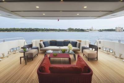 Luxurious outdoor seating on a yacht deck offers a serene view of a distant coastline with a historic fortress.