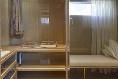 A minimalist closet features a hanging scarf, neatly folded blankets, and a plush bench against a backdrop of sheer curtains.