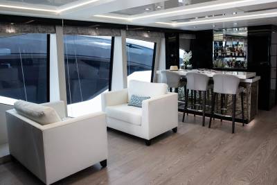 Relax in the plush white seating area of this luxurious yacht's salon, complete with a well-stocked bar and stunning ocean views.