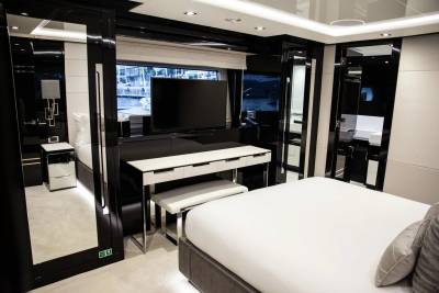 A luxurious yacht cabin features a sleek black and white design with a large television, vanity, and comfortable bed overlooking the water.