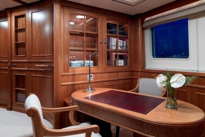 An elegant wood-paneled office aboard a yacht features a classic desk, comfortable seating, and a window overlooking the night sea.