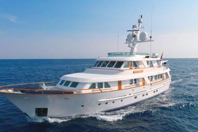 A classic white motor yacht cruises through the deep blue ocean under a clear sky.