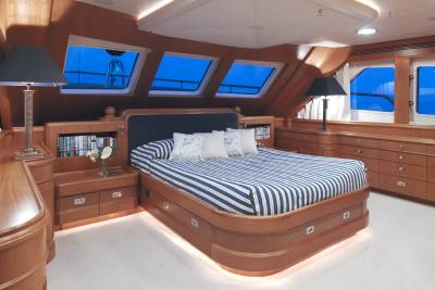 Luxurious yacht cabin features a striped bed, built-in bookshelves, and large windows offering ocean views.