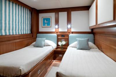 Two twin beds with light blue headboards and white striped linens are nestled within a wood-paneled cabin.