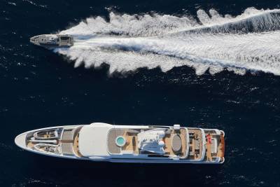 A sleek superyacht glides through the deep blue ocean, leaving a powerful wake behind a smaller, fast-moving vessel.