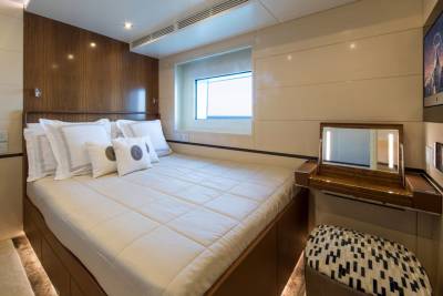 A luxurious yacht cabin features a comfortable bed, a vanity with a lighted mirror, and a television displaying a mountain landscape.
