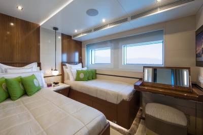 Luxurious twin beds with plush green pillows are perfectly arranged in this elegant yacht cabin.