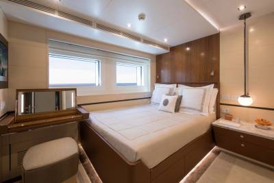 Luxurious yacht cabin features a comfortable bed, a vanity with a lighted mirror, and large windows overlooking the sea.