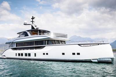 A sleek white superyacht glides through calm turquoise waters with majestic mountains in the background.