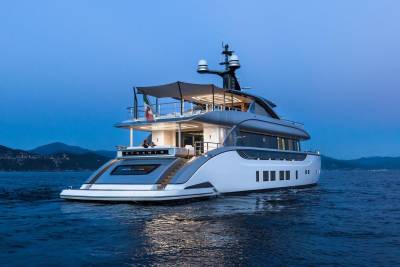 A luxurious yacht named Dynamiq cruises on calm waters under a twilight sky, with distant hills providing a scenic backdrop.