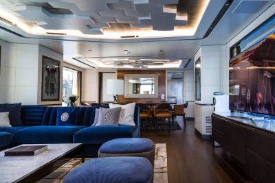 Luxurious yacht interiors feature plush blue seating and a modern ceiling design overlooking a scenic landscape.