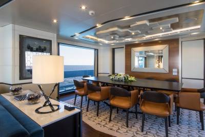 A modern dining area with a large table and plush seating offers stunning ocean views through a panoramic window.