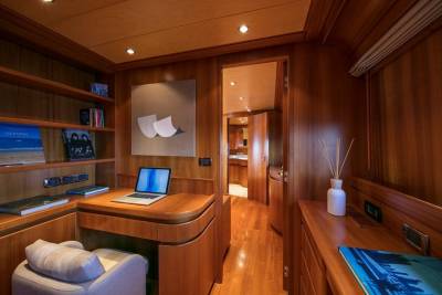 A cozy wooden study nook on a yacht features a laptop, books, and a comfortable chair.