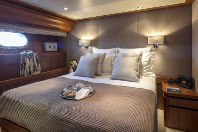 A luxurious yacht cabin offers a cozy retreat with a neatly made bed, a tray of coffee and cookies, and a porthole view.