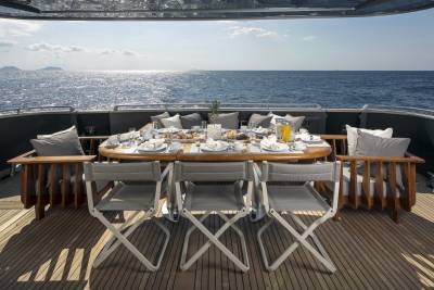 A beautifully set breakfast table awaits on the deck of a yacht, overlooking the sparkling blue ocean.